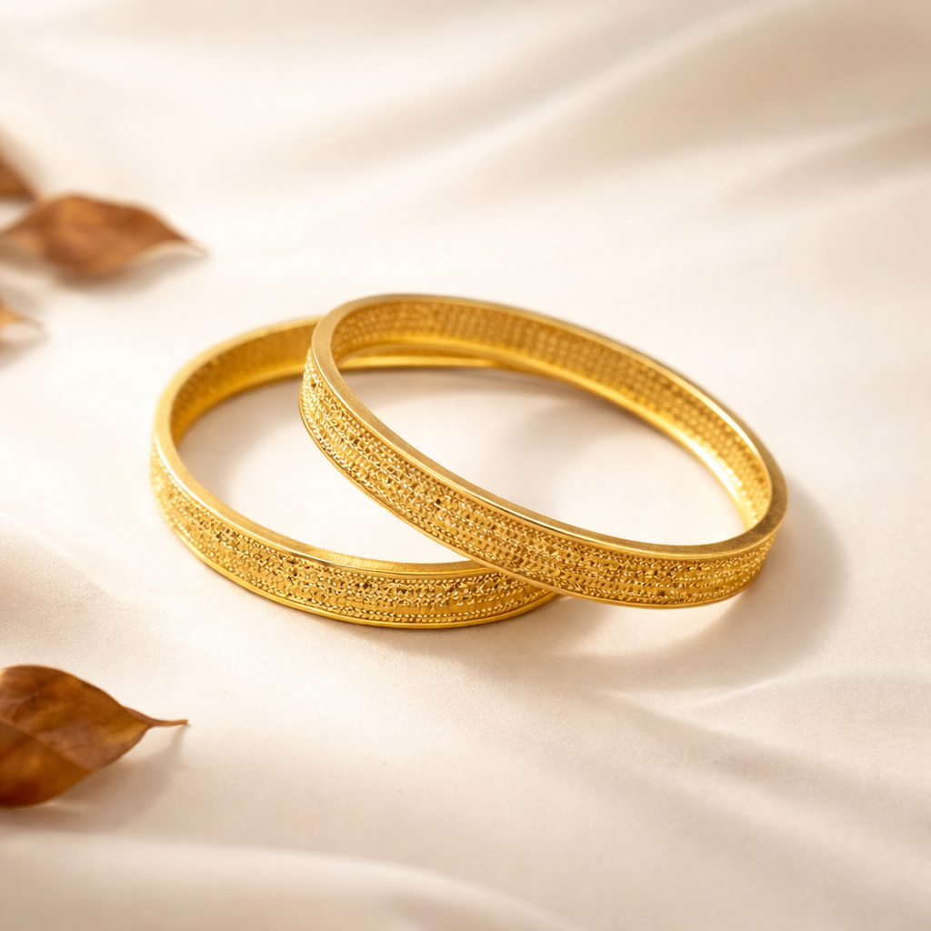 Two gold bangles on a beige fabric background with leaves.