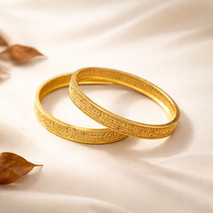 Two gold bangles on a beige fabric background with leaves.