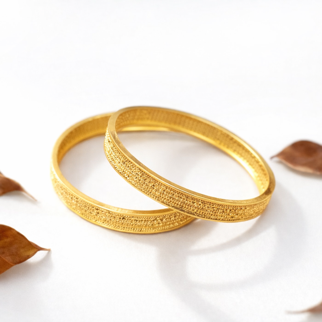 Two gold bangles on a white surface with leaves in the background