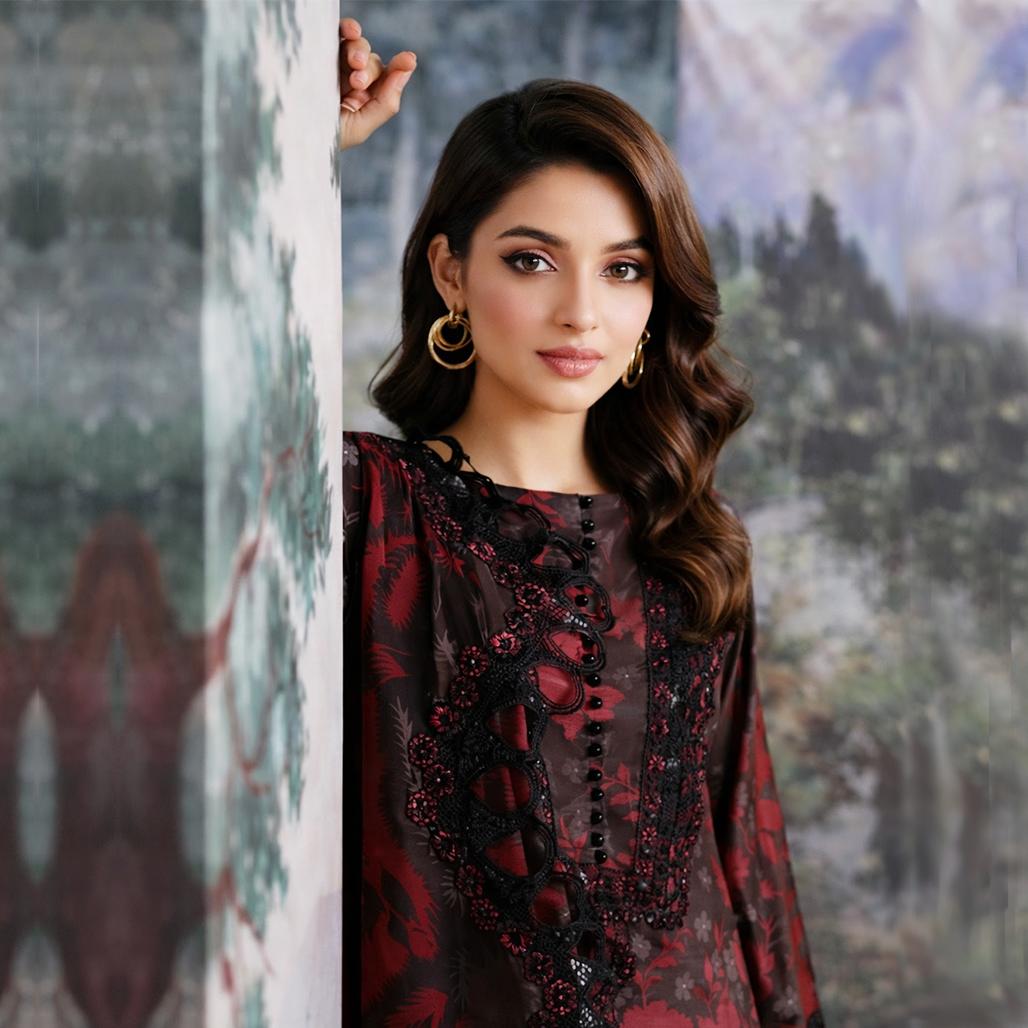 Woman in a red and black embroidered outfit standing against a textured wall.