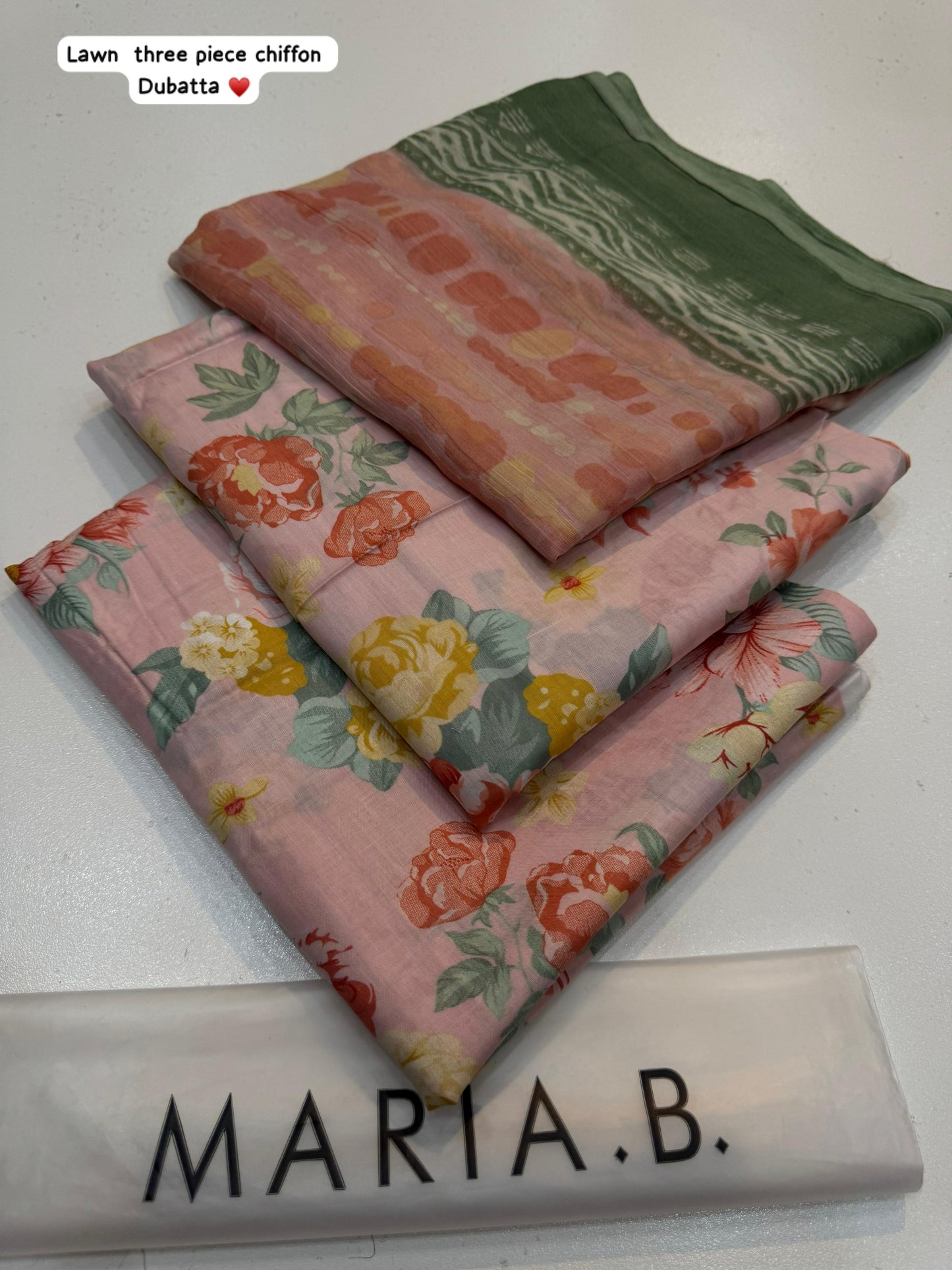 Three pieces of fabric with floral patterns stacked on a white surface, branded 'Maria B'.